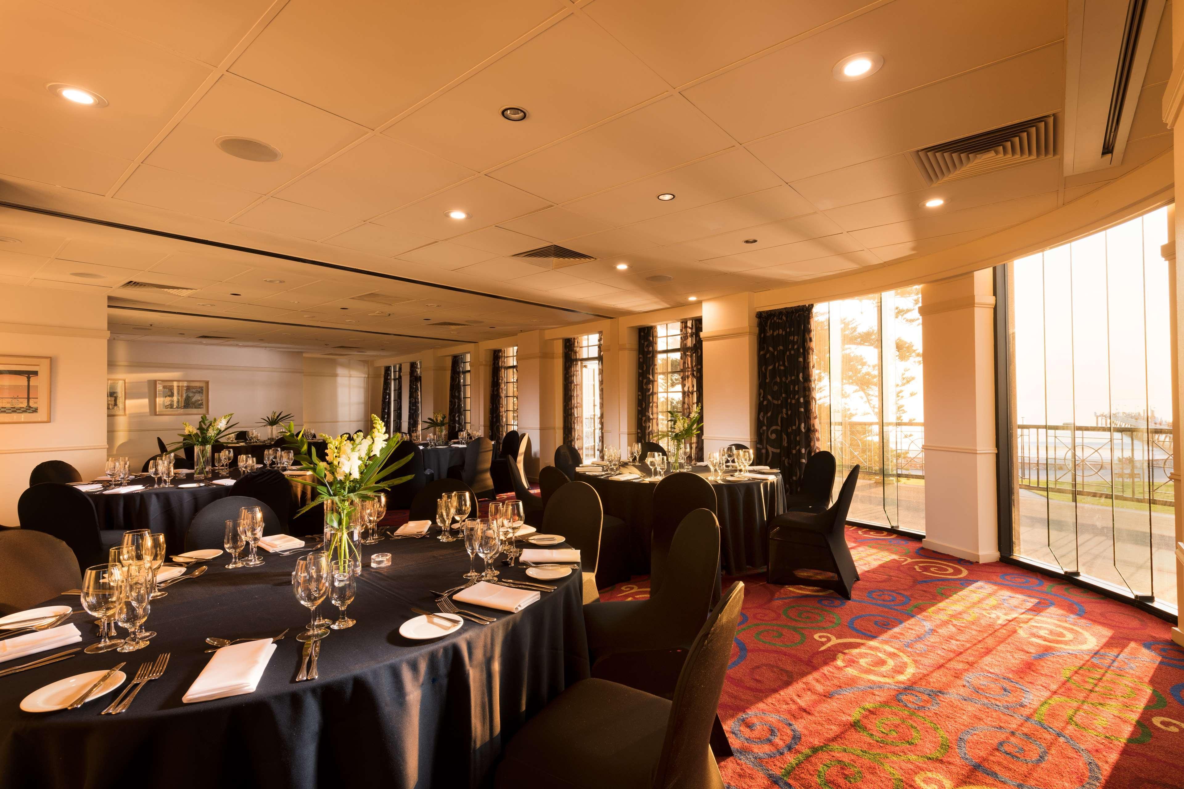 Hotel Stamford Grand Adelaide Glenelg Zewnętrze zdjęcie The photo shows a well-decorated event space or dining area. There are several round tables draped in dark tablecloths, each set with elegant dinnerware, including glasses and cutlery. The room features large windows that allow natural light to flood