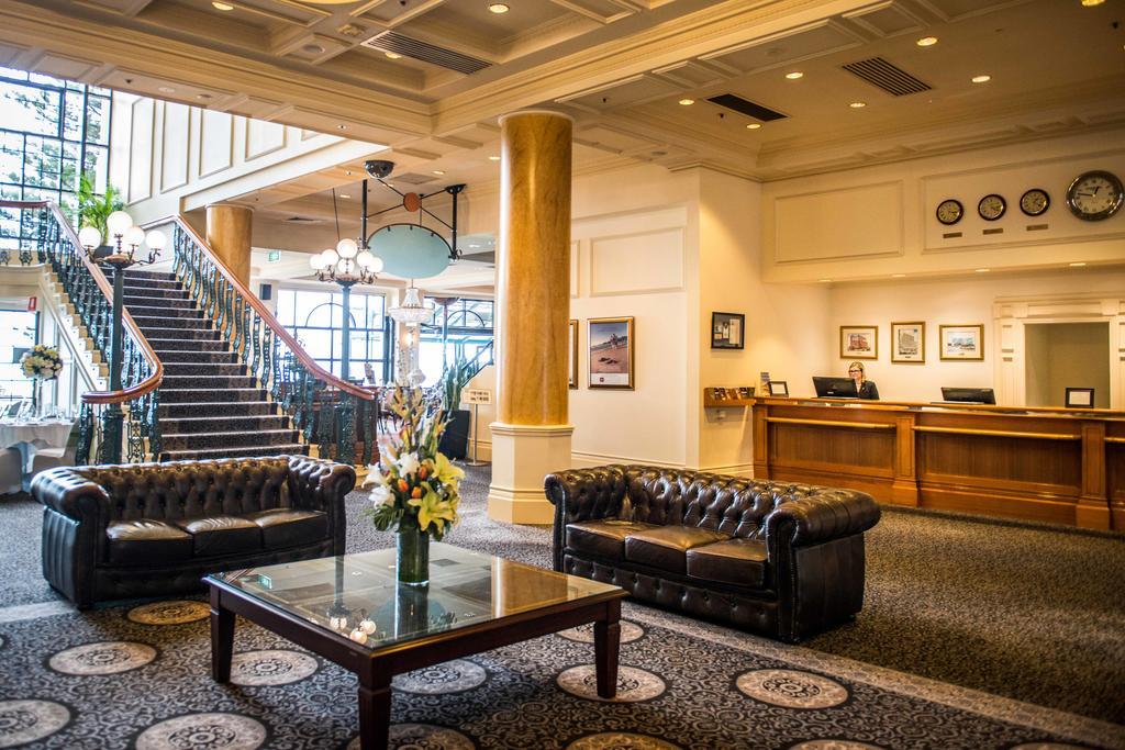 Hotel Stamford Grand Adelaide Glenelg Zewnętrze zdjęcie The photo depicts a hotel lobby featuring a spacious and elegant design. There are two dark leather sofas arranged in front of a glass coffee table, adorned with a floral centerpiece. The lobby has a refined atmosphere, highlighted by large windows t