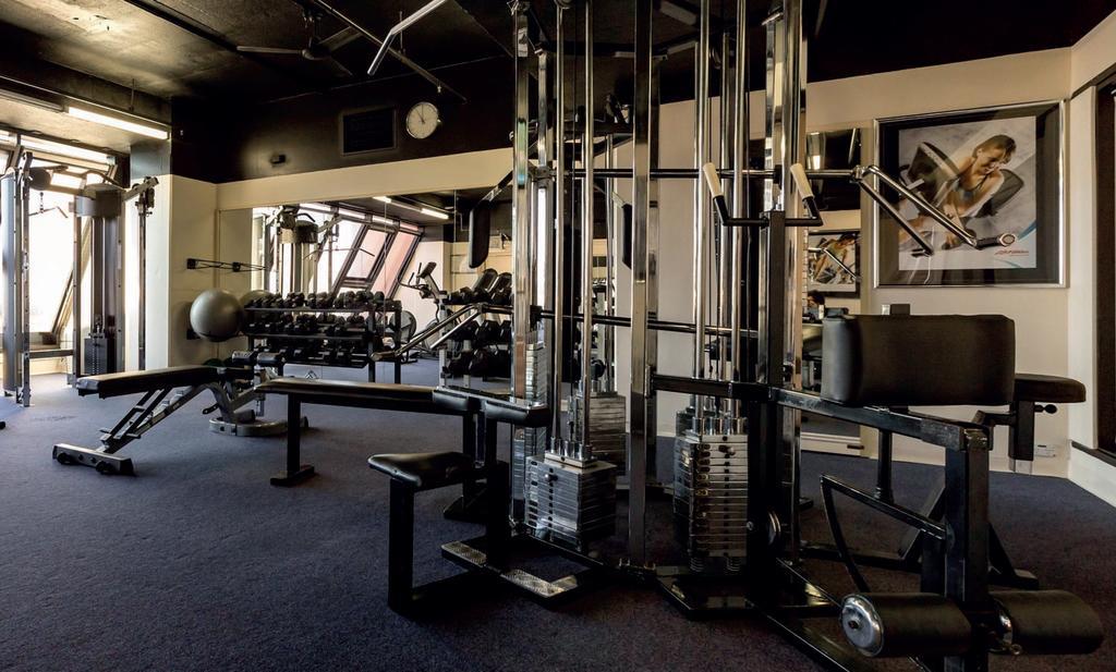 Hotel Stamford Grand Adelaide Glenelg Zewnętrze zdjęcie The photo shows a gym interior with several pieces of exercise equipment. In the foreground, there is a multi-station machine that features various pulleys and weights. To the side, there are benches and free weights, including dumbbells. The gym has